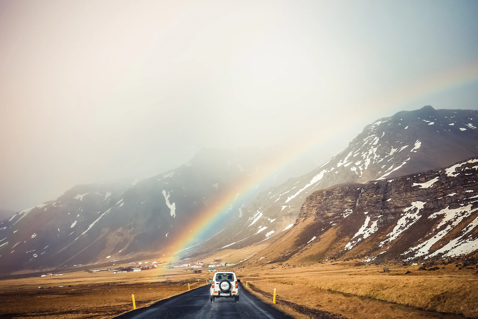 A car parked off the road beneath a rainbow in Iceland