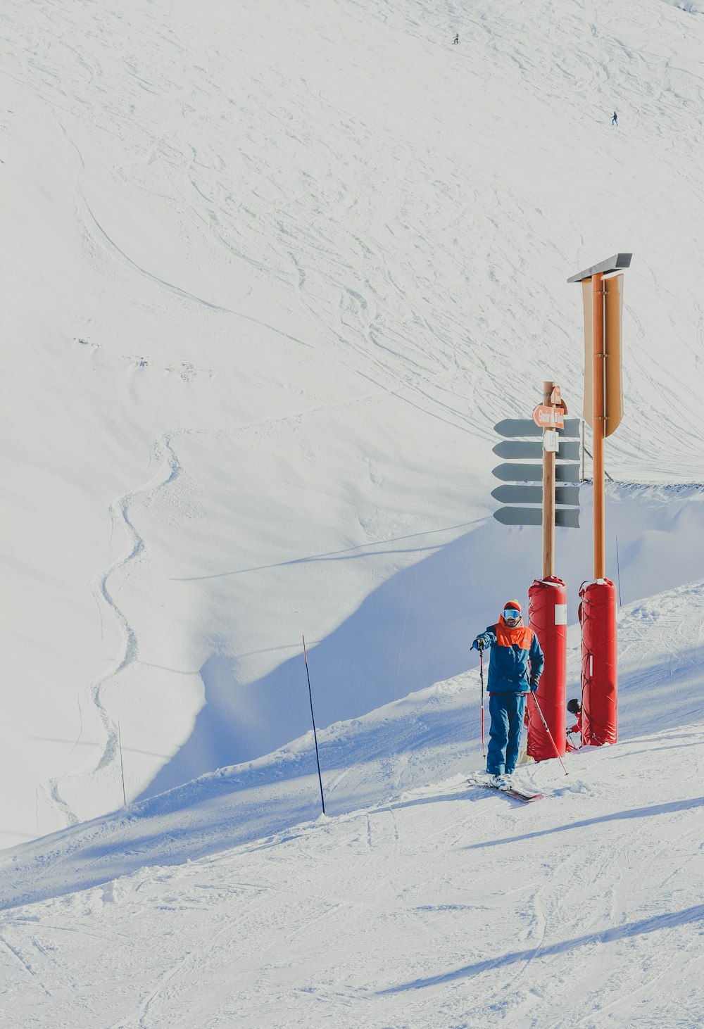 赤と茶色の支柱のそばに立つスキーストックを持つ青いジャケットの男