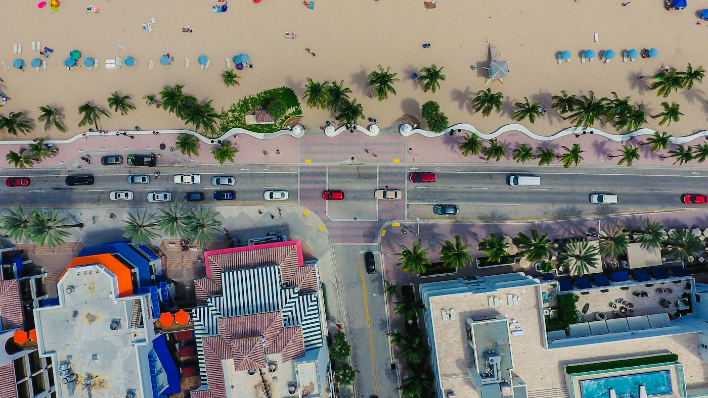 A beachfront road, palms and sand from above on Broward County’s coast.