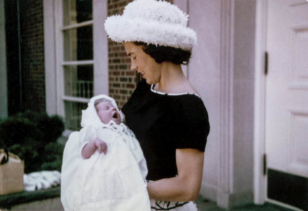 mulher que carrega o bebê em pé perto da porta de madeira branca