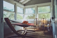photography of grey, white, and brown wooden house interior with three brown wooden Windsor chairs beside brown hammock with glass windows