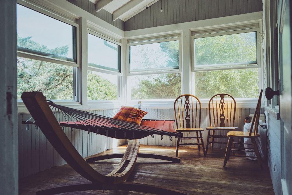 photography of grey, white, and brown wooden house interior with three brown wooden Windsor chairs beside brown hammock with glass windows