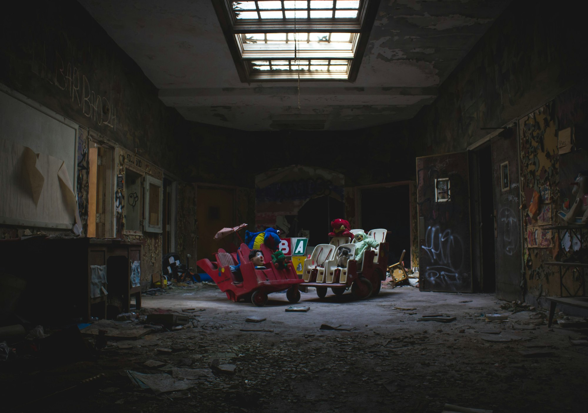 An abandoned asylum corridor with peeling walls and toys in the middle of the room.