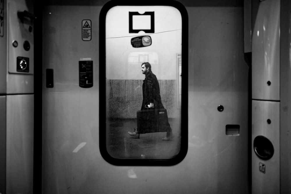 man walking outside train door in grayscale photo