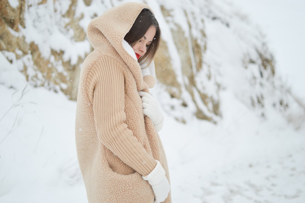昼間、雪に覆われた茶色の岩のそばに立つ茶色のコーデュロイのフード付きコートを着た女性