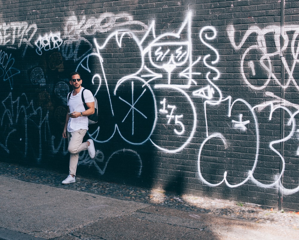 man wearing white crew-neck T-shirt leaning on black wall with white graffiti