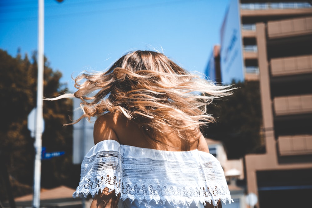 Foto di donna che indossa un crop top bianco con spalle scoperte in piedi accanto a un edificio in cemento sotto il cielo azzurro