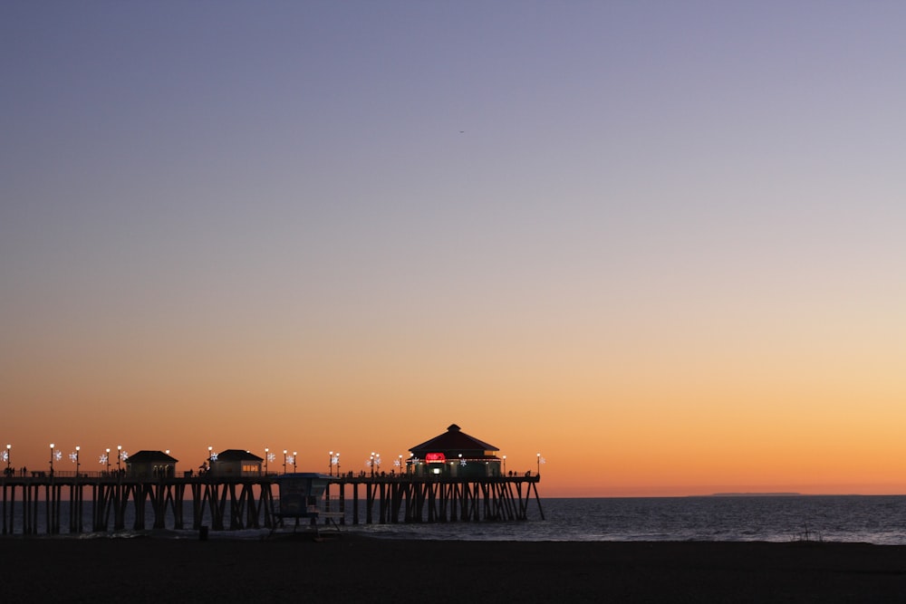 silhouette photo of boardwalk with cottage on body of water