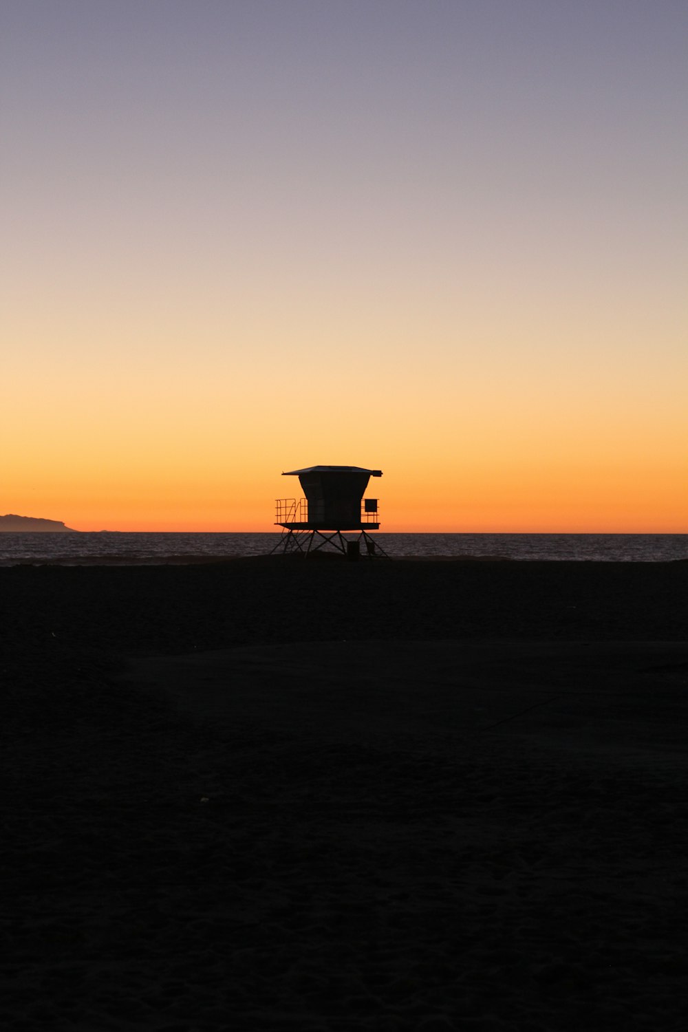 silhouette photo of shed on sand near sea during golden hours