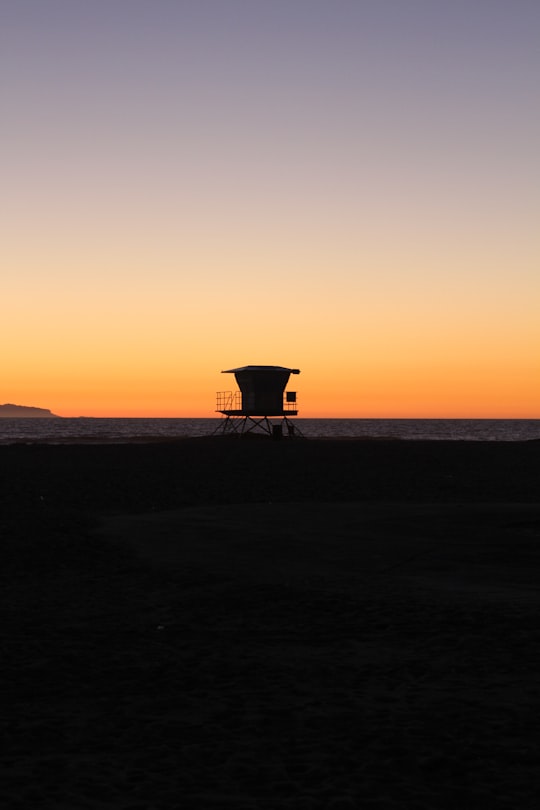 silhouette photo of shed on sand near sea during golden hours in Huntington Beach United States