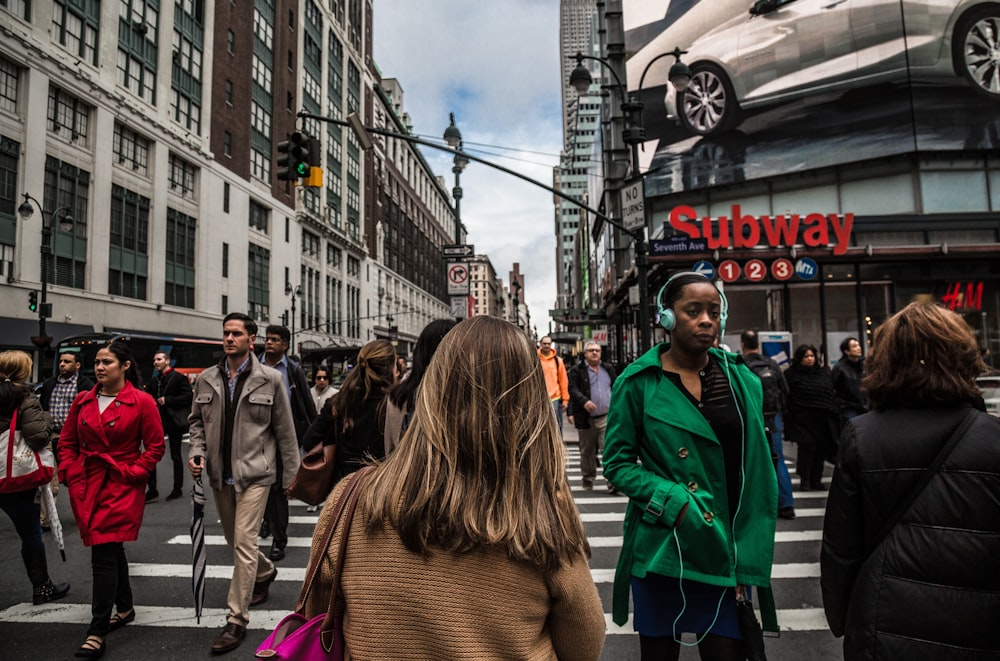 woman wearing green jacket walking on the pedestrian lane during daytime