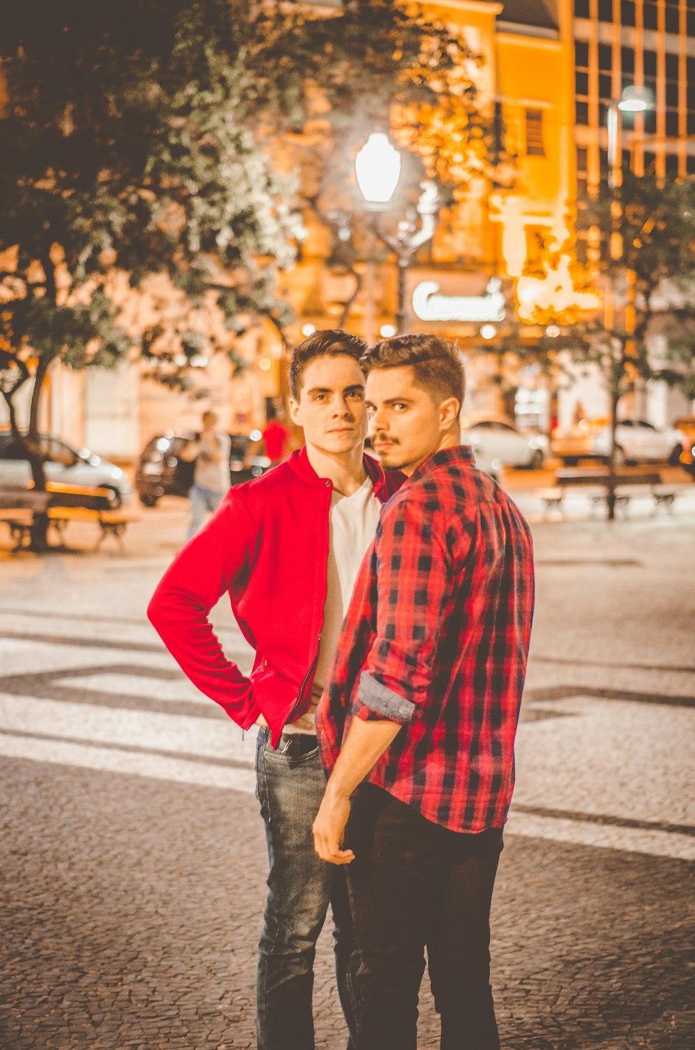 Two young men standing close together at night in a city square