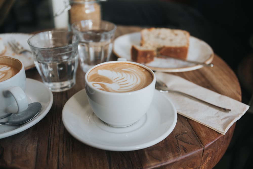 weißer Keramikbecher auf weißer Keramikuntertasse auf braunem Holztisch