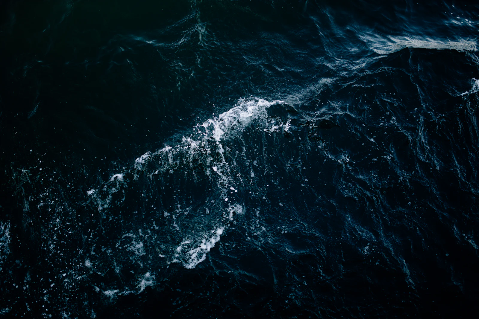 Dark open water breaking into foam, seen from above.