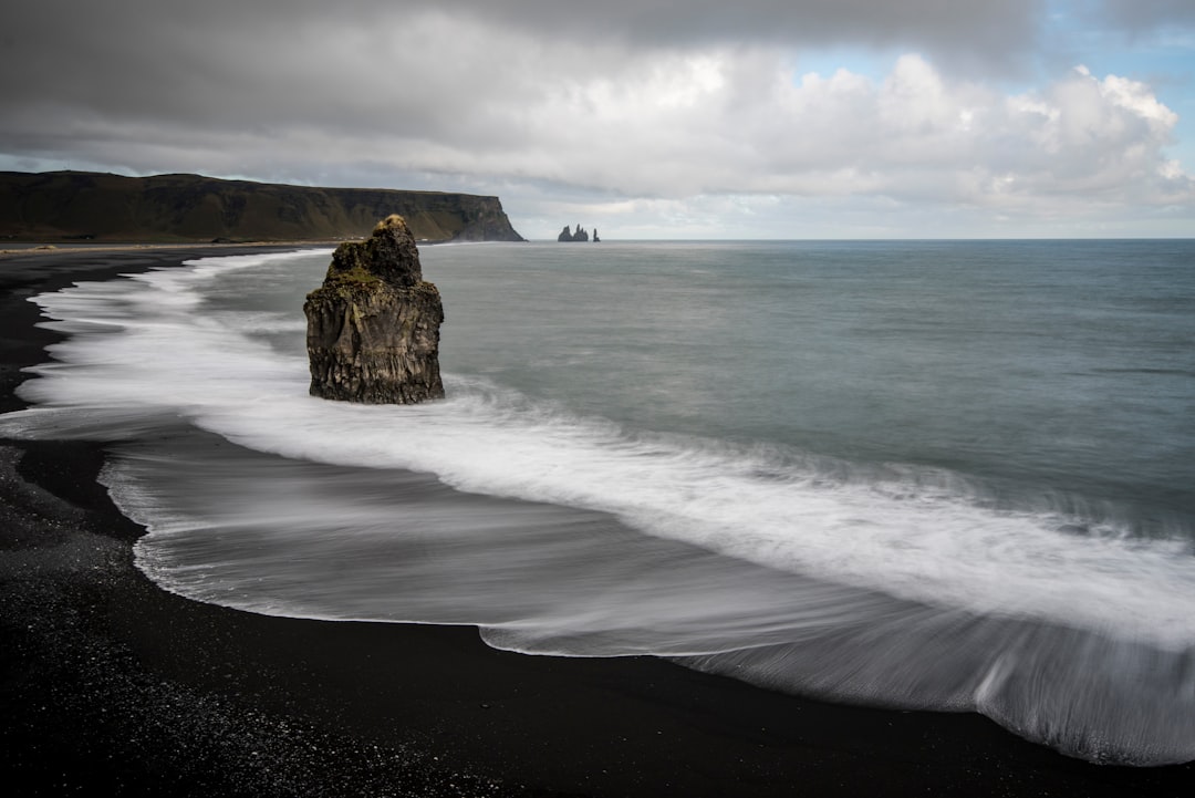 brown rock on seashore under white clouds at daytime