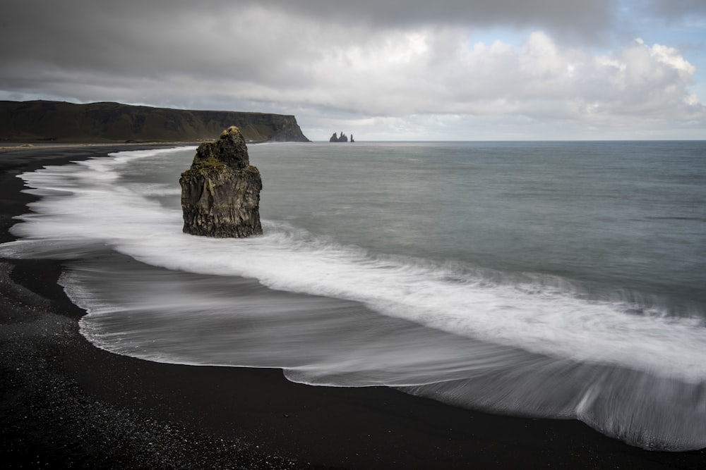 brown rock on seashore under white clouds at daytime