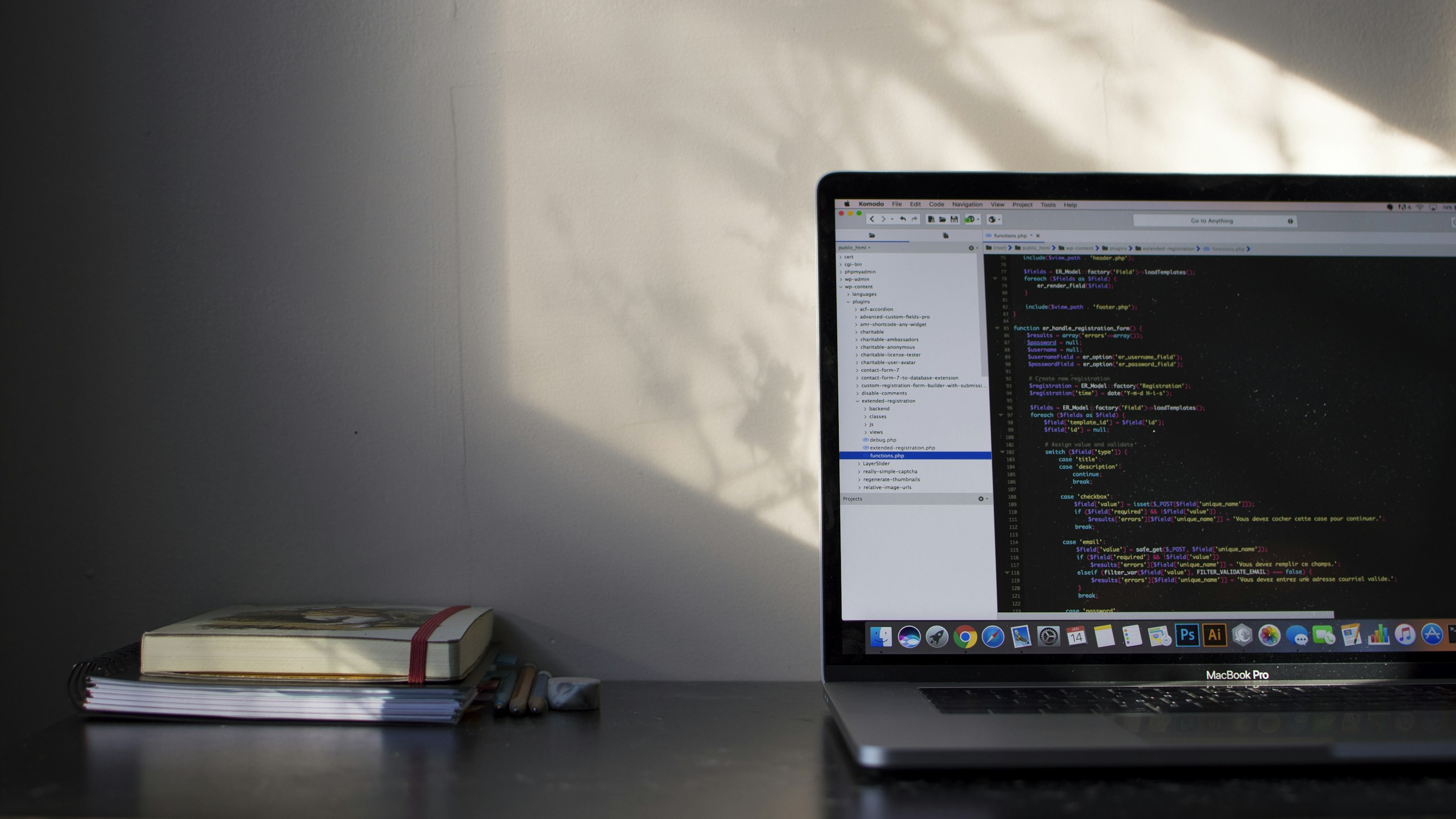 A laptop with code on the screen, and a desk in-front of a white wall.