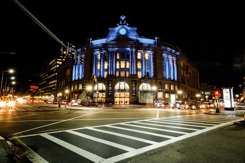blue and white concrete building on cross roads with pedestrian lane at night time