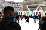 man wearing black backpack ice skating with other people near Toronto freestanding decor during daytime