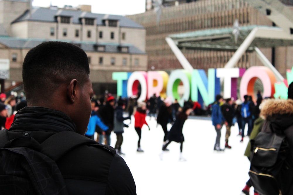 uomo che indossa uno zaino nero che pattina sul ghiaccio con altre persone vicino all'arredamento indipendente di Toronto durante il giorno