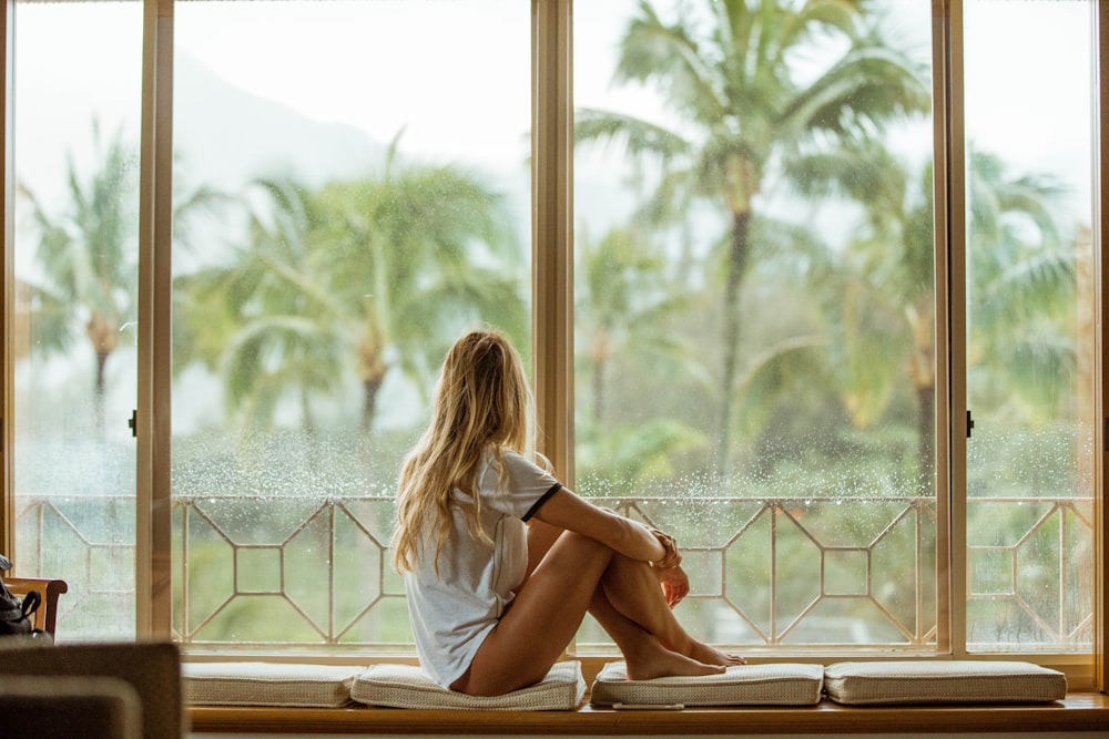 woman sitting on white cushion near glass window