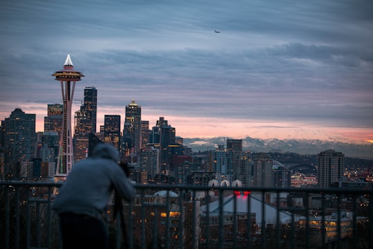 photo of person wearing grey pullover hoodie taking a photo of concrete buildings under cloudy sky in Seattle United States