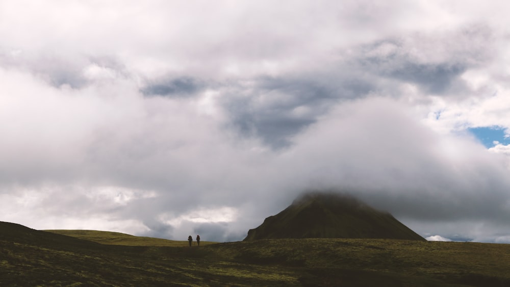 two person walking through mountain under clouds formation