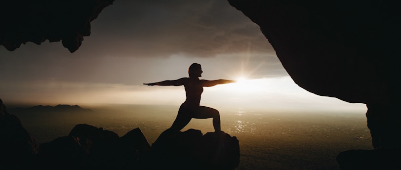 silhouette of person in yoga post on top of cliff during sunset