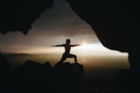 silhouette of person in yoga post on top of cliff during sunset