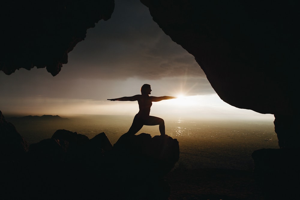 Silhouette einer Person im Yoga-Pfosten auf einer Klippe während des Sonnenuntergangs