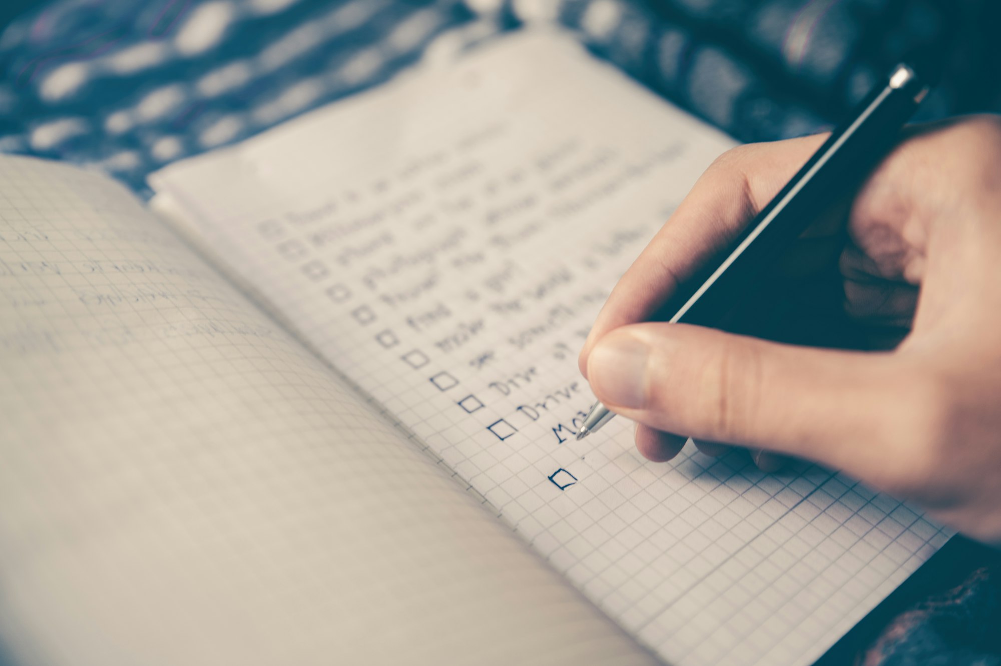 A checklist of items, written in a notebook, with a hand holding a pen about to check one of the boxes.