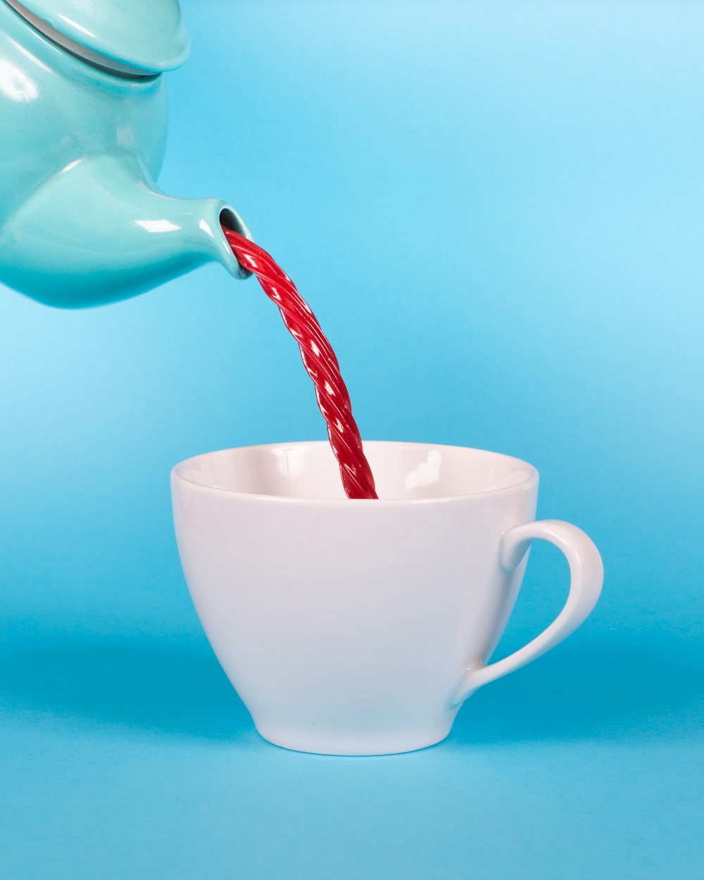 tetera verde vertiendo líquido rojo a la fotografía de primer plano de la taza de té blanca