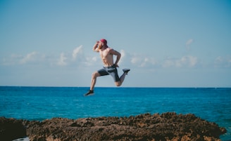 man jumping in mid air while looking ahead beside body of water during daytime