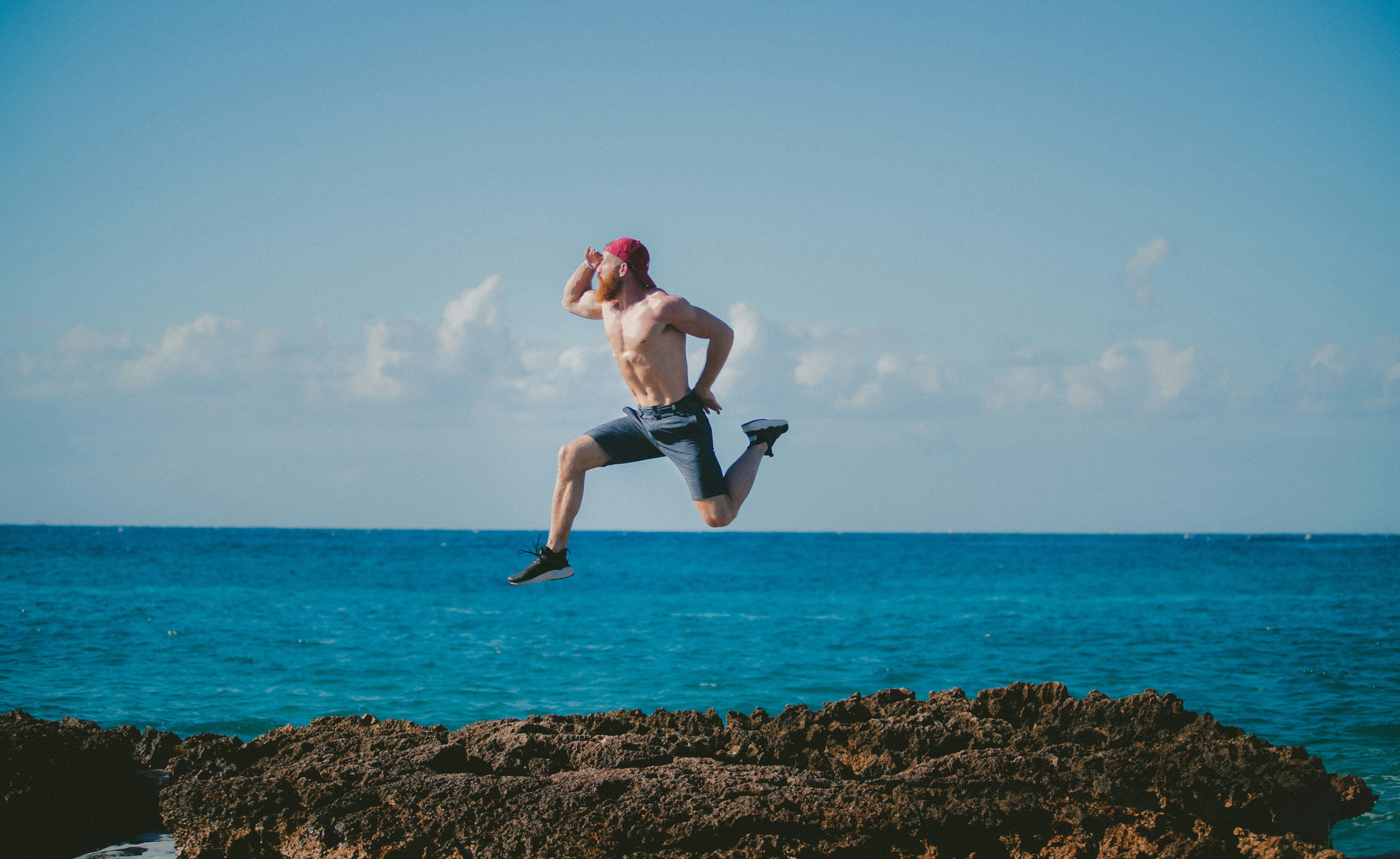 man jumping in mid air while looking ahead beside body of water during daytime