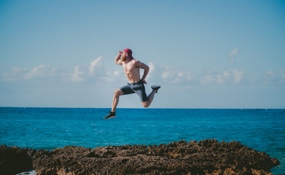 man jumping in mid air while looking ahead beside body of water during daytime