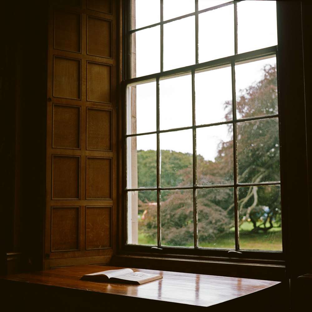 white open book on brown wooden table in front of clear glass window in dim room