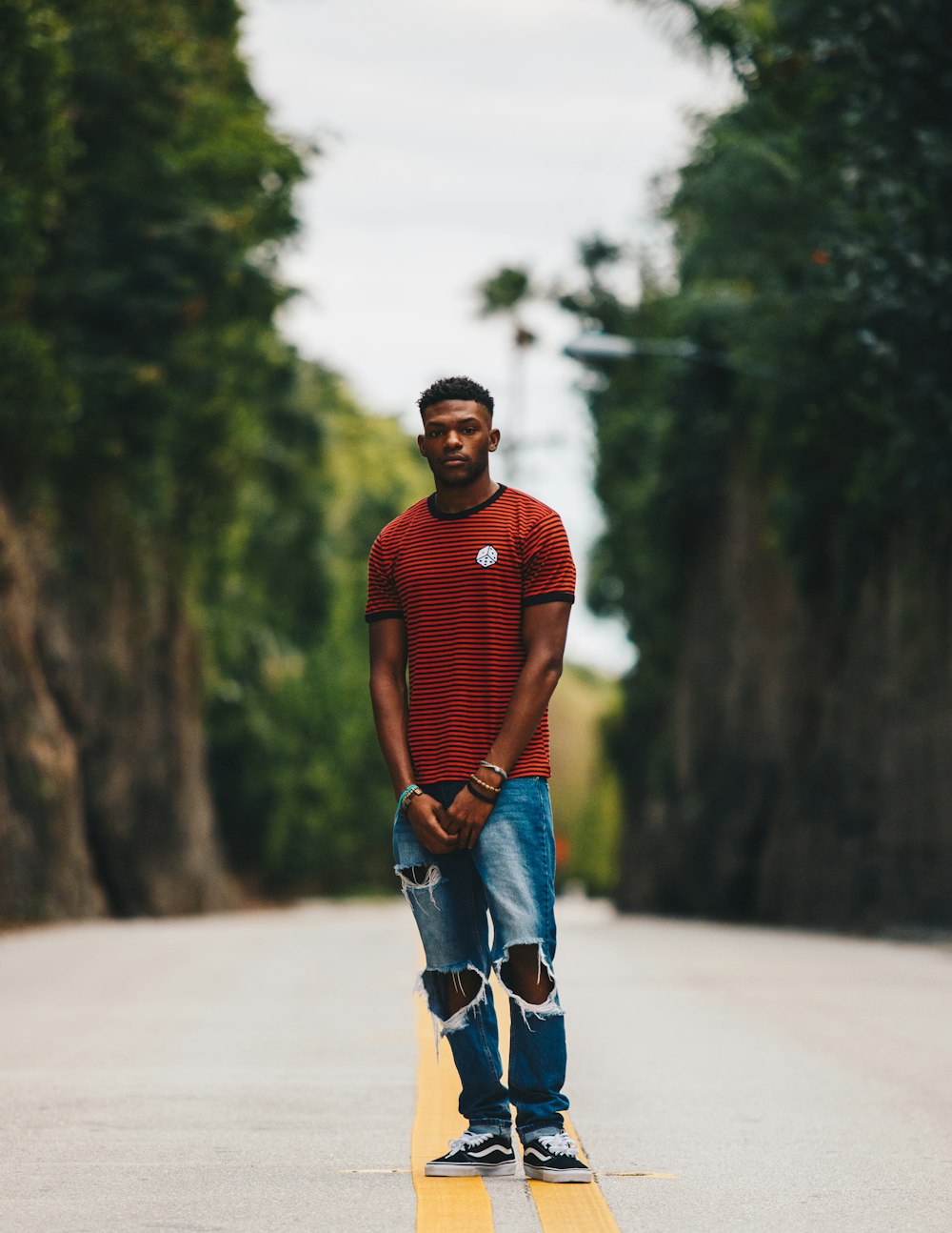 man in red shirt and blue distress denim jeans standing in middle of road