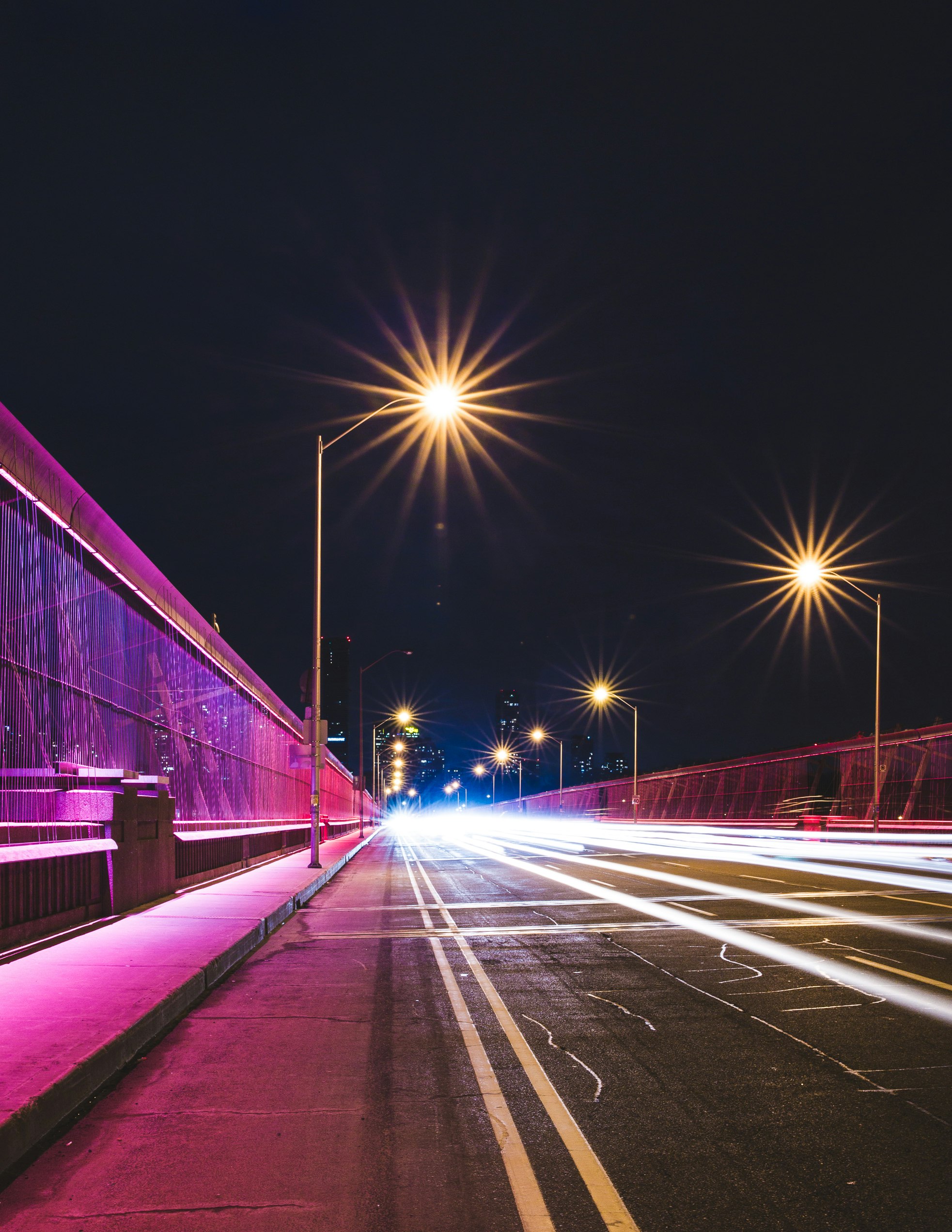 black concrete road between post lamps under black sky at nighttime