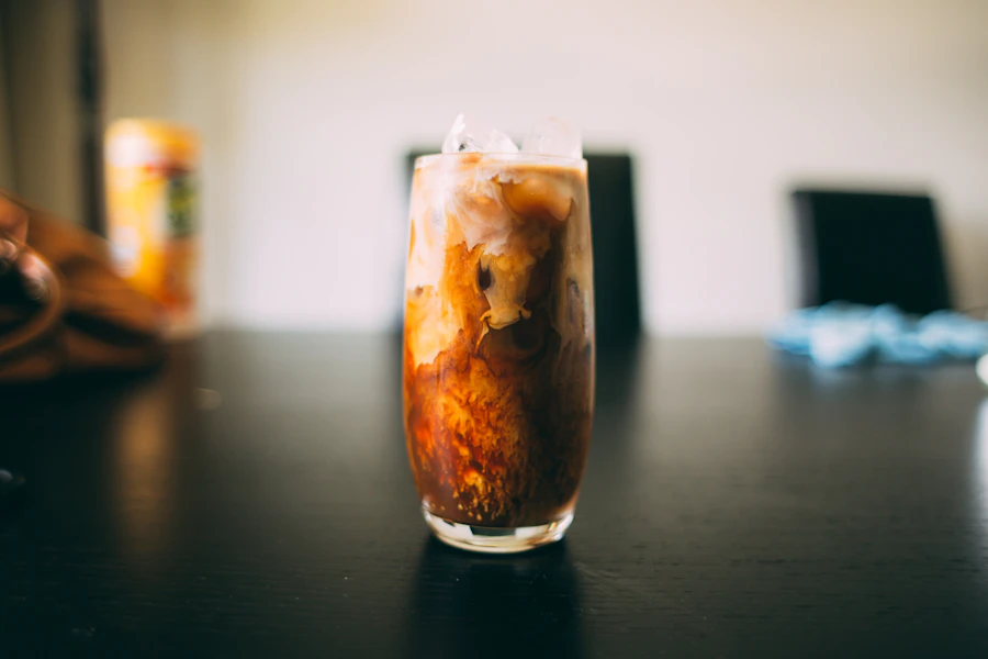 Iced coffee with milk swirling through it in a tall glass on a dark counter