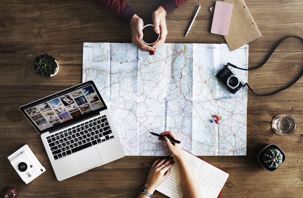 top-view photography of persons holding mug and pen using MacBook and world map