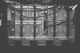 A monochrome photograph of a server rack with multiple units. The image shows intricate patterns of ventilation grids and various cables connected to the hardware. Small indicator lights suggest the equipment is operational.