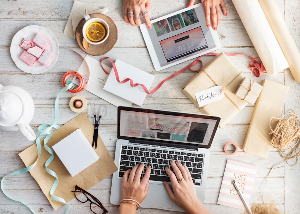 person using MacBook and iPad surrounded by papers and boxes top-view photograhpy