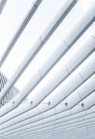 A modern architectural design featuring overlapping linear panels with clean, sharp lines. The perspective emphasizes symmetry and repetition, creating a sense of depth. The panels are primarily gray and white, contributing to a minimalistic aesthetic.