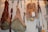 Various types of cured meats, including sausages, hams, and a packaged pancetta, are hanging from hooks. The meats are arranged on a wall, showing a rustic and artisanal display. Cooking tools with wooden handles are also hanging next to the meats.