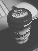 A black and white image of a Mentos Pure Fresh sugar-free gum container with visible branding. It is placed on a dark surface with a blurred background that appears to be part of a keyboard.