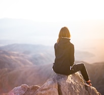 person sitting on top of gray rock overlooking mountain during daytime