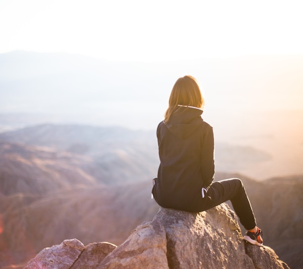 person sitting on top of gray rock overlooking mountain during daytime