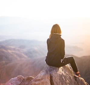 person sitting on top of gray rock overlooking mountain during daytime