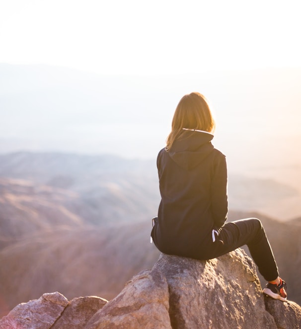 person sitting on top of gray rock overlooking mountain during daytime