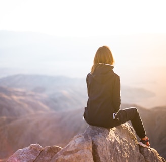 person sitting on top of gray rock overlooking mountain during daytime